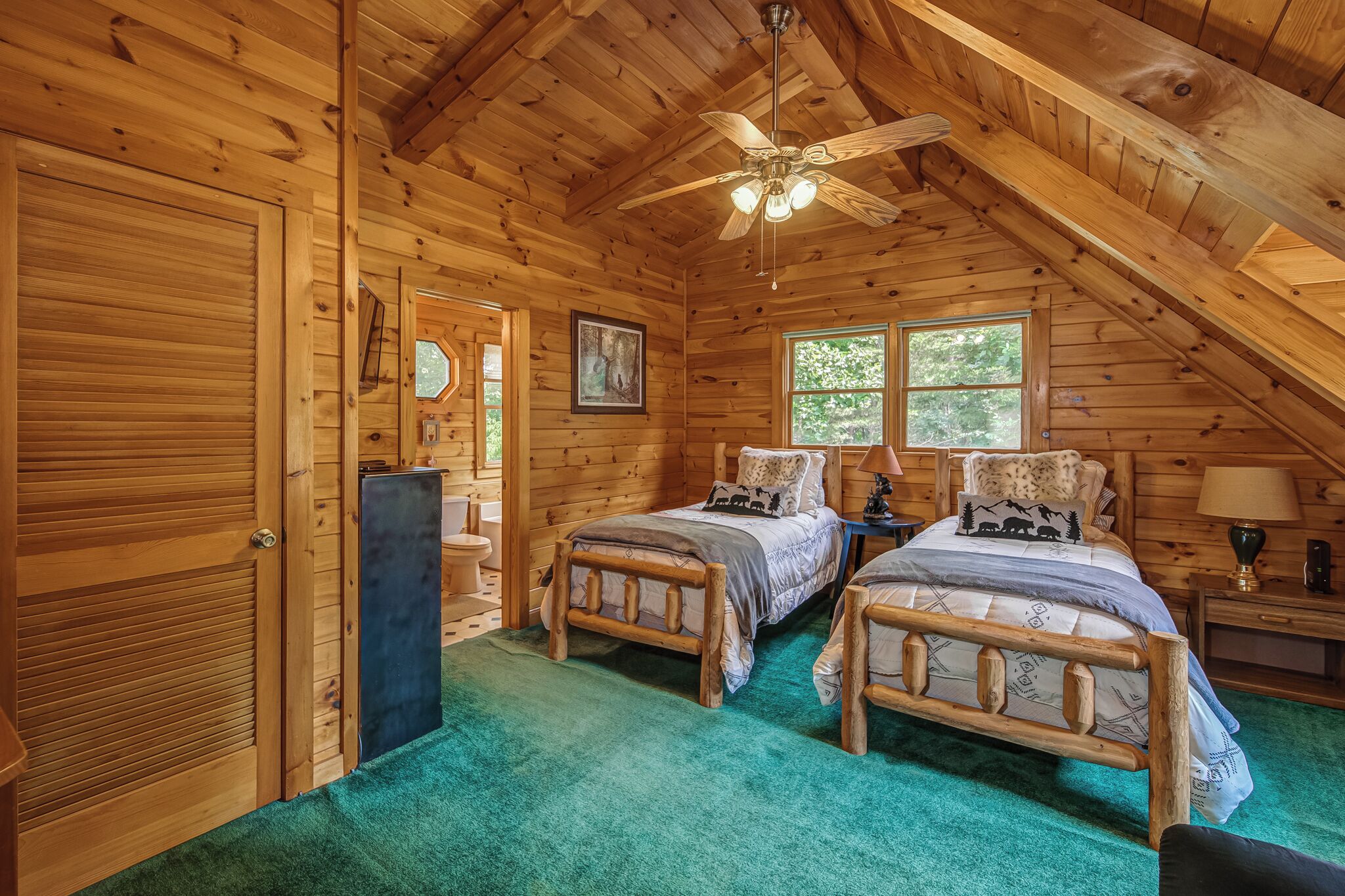 A log cabin bedroom with two beds, a ceiling fan, and a window.