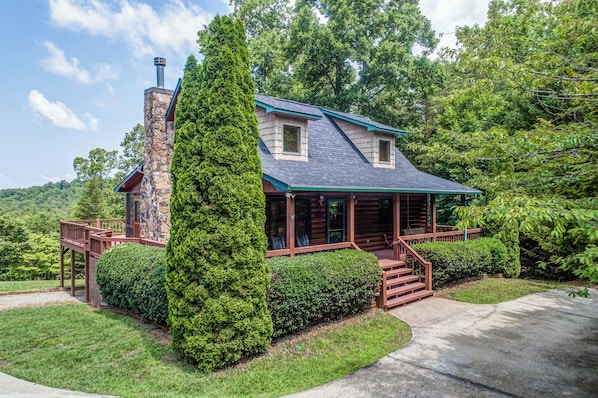 A log cabin with a stone chimney, wooden deck, and a well-maintained lawn.