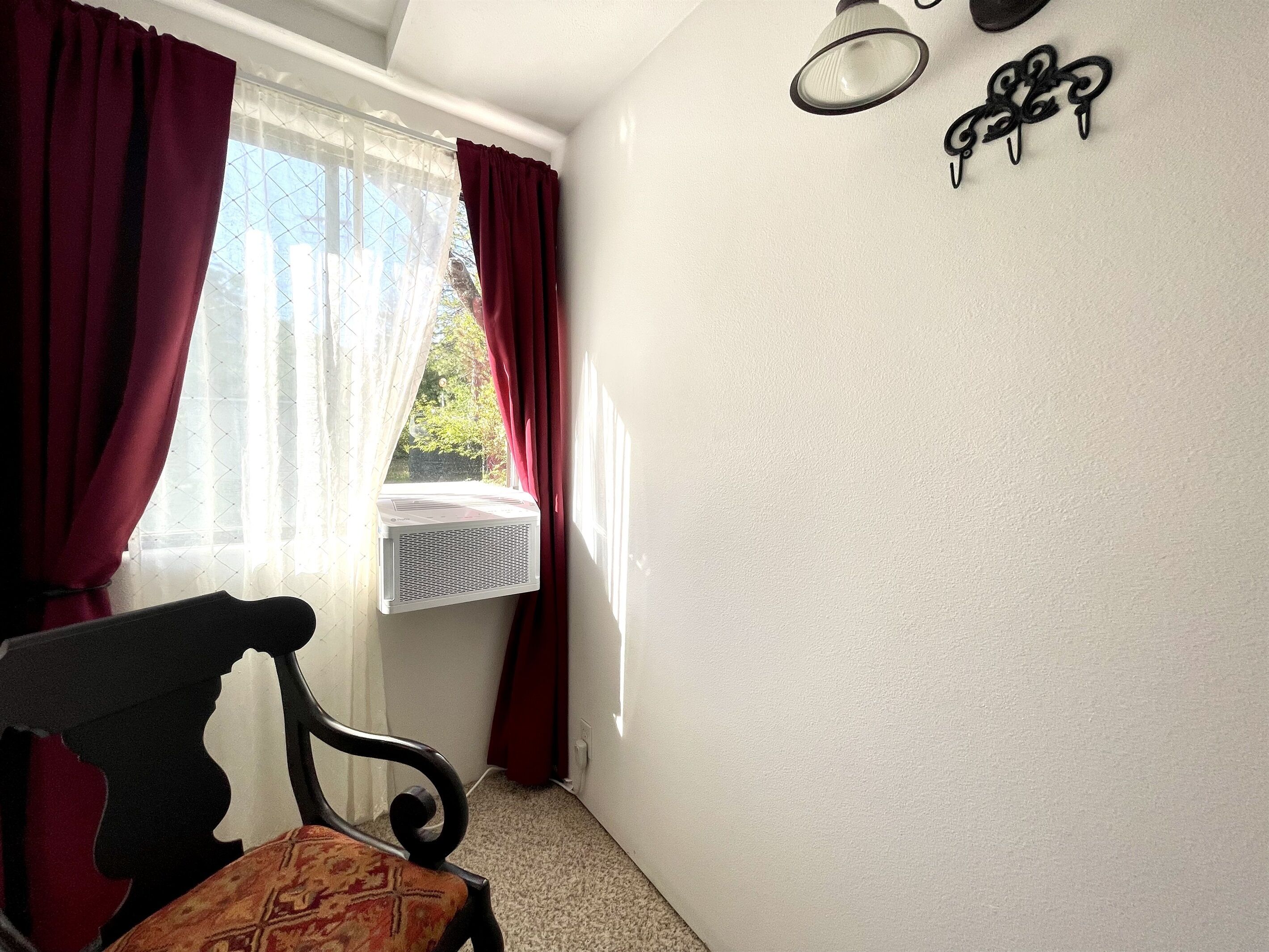 Una habitación con ventana, un radiador, una silla y una lámpara fijada a la pared.