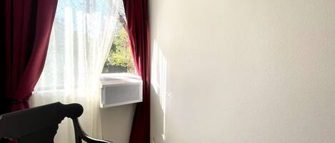 Una habitación con ventana, un radiador, una silla y una lámpara fijada a la pared.