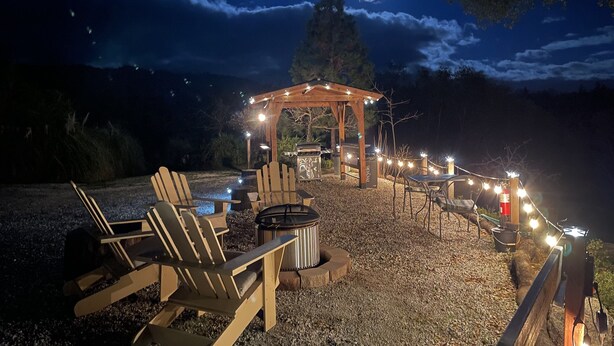 An outdoor seating area with Adirondack chairs and a wooden pergola, surrounded by string lights. - Sunrise Suite - Sierra Mountain Lodge (Ahwahnee)
