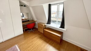 Une petite pièce moderne avec un plafond en pente, un bureau en bois, une chaise rouge et une fenêtre avec des rideaux.