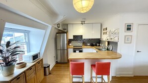 Une cuisine moderne dotée d’un îlot central, de meubles en bois, d’un réfrigérateur en acier inoxydable et d’un luminaire suspendu.