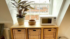 Une cuisine avec un meuble en bois, un four à micro-ondes, une plante en pot et une vue sur des immeubles par la fenêtre.