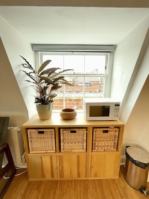 Kitchen area with a microwave, wicker baskets, and a potted plant.