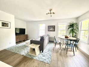 A spacious living room with a grey sofa, a wooden coffee table, and a dining area with a round table and chairs. - Brunswick Downtown Sugar Cube next to Bowdoin (Brunswick)