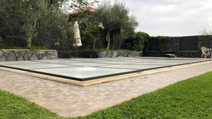 Una piscina rettangolare con bordo piastrellato, circondata da un muro in pietra e vegetazione.