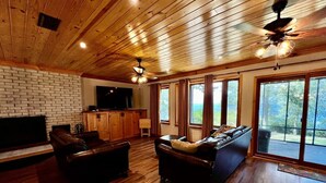 A spacious living room with a fireplace, leather sofas, and large windows offering a view of the outdoors. - Poco's Retreat                                . (Many)