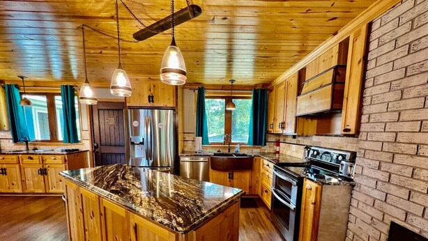 A spacious kitchen with wooden cabinets, a granite countertop island, stainless steel appliances, and a brick wall. - Poco's Retreat                                . (Many)