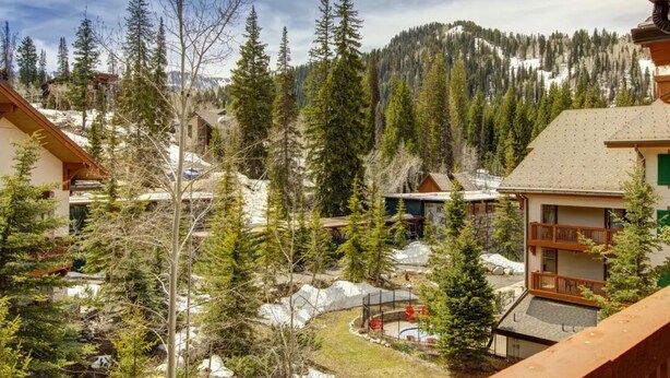 Un chalet de montagne composé de plusieurs bâtiments, entouré d’une forêt dense et d’un sol recouvert de neige.