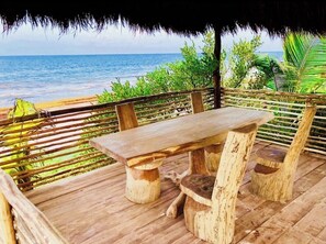 Een houten terras met een tafel en stoelen, met uitzicht op een strand en de oceaan.