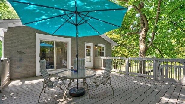 A wooden deck with a glass table and chairs, a turquoise umbrella, and a white railing. - White Oak 4BR @ Patterson Place (Durham)