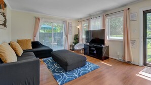 A modern living room with a black sofa, ottoman, and entertainment unit. - White Oak 4BR @ Patterson Place (Durham)