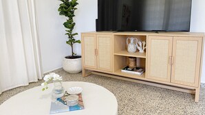 Un salon avec un téléviseur posé sur un meuble en bois, une plante en pot et une table basse ronde sur laquelle se trouvent des livres et des objets décoratifs.