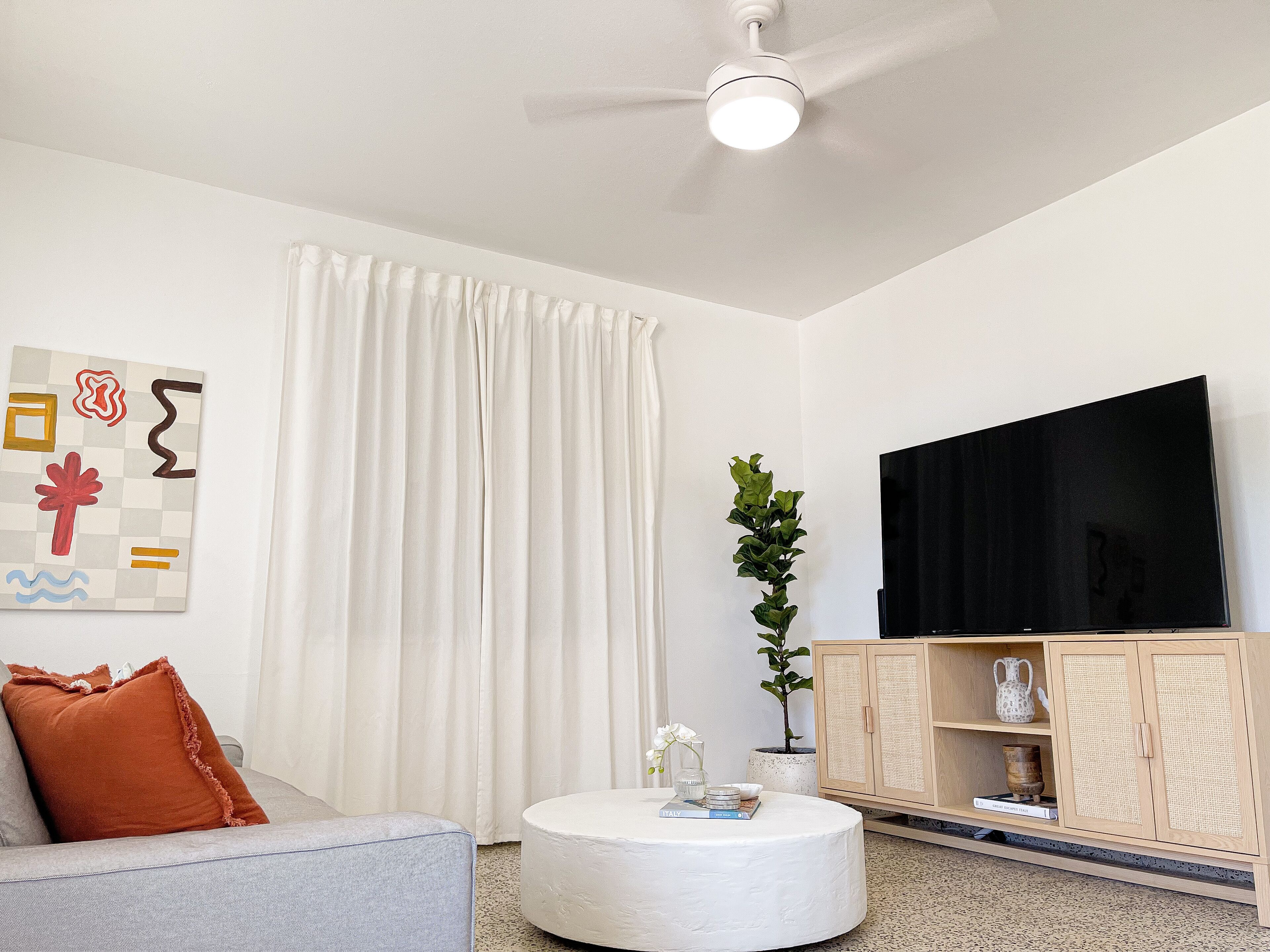 Una sala de estar moderna con un sofá, una mesa de centro redonda, un televisor de pantalla plana y un mueble de madera.