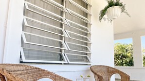 Une pièce meublée de meubles en osier, avec une grande fenêtre et une plante suspendue.