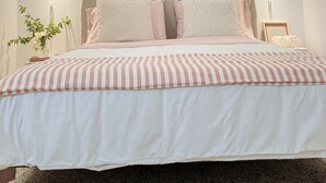 Un lit bien fait, recouvert d’une couvre-lit à rayures, deux lampes fixées au mur et un vase rempli de fleurs sur la table de chevet.