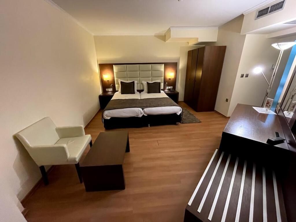 A modern hotel room with a large bed, a desk, a chair, and a wardrobe.