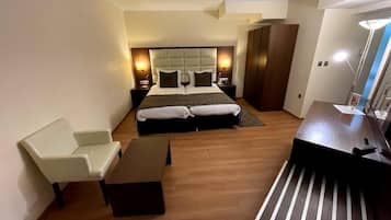 A modern hotel room with a large bed, a desk, a chair, and a wardrobe.
