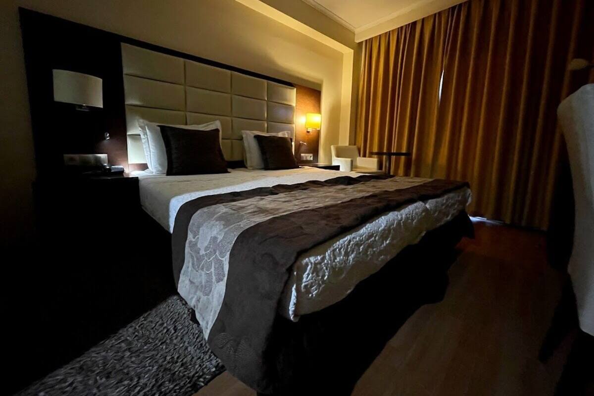 A hotel room with a large bed, a headboard with a light panel, a bedside table, and a curtain.