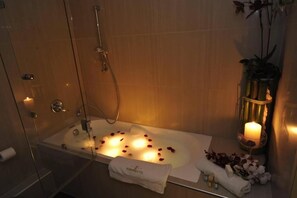 A modern bathroom with a glass-enclosed bathtub, a handheld showerhead, and a lit candle on a side table. - Europa Hotel (Kastoria)