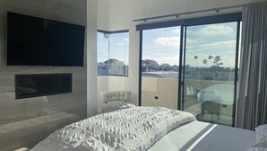 Een moderne slaapkamer met een groot bed, een flatscreen televisie en een balkon met uitzicht op de stad.