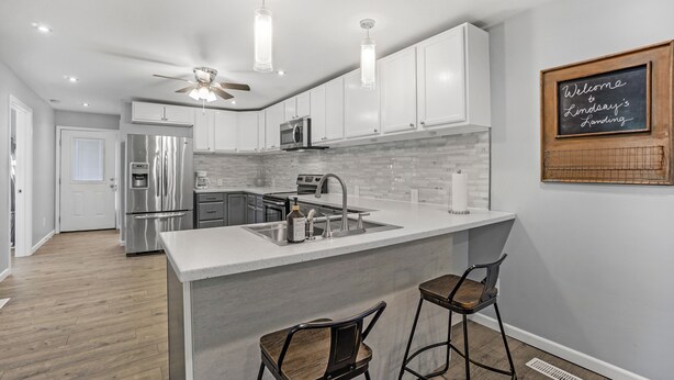 A modern kitchen with white cabinets, stainless steel appliances, and a bar area with stools. - Clean, comfortable home. (Marion)