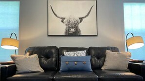 A black leather sofa with two pillows, a wooden coffee table, and a framed artwork of a yak on the wall. - Clean, comfortable home. (Marion)