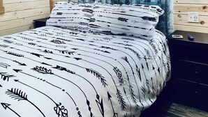 Habitación con paneles de madera, una cama, una mesita de noche y una lámpara fijada a la pared.