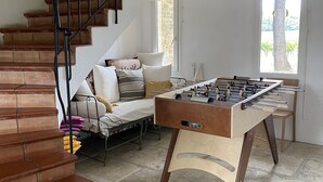 A cozy living room with a wooden staircase, a sofa with cushions, and a foosball table. - Family home amidst vineyards in Drôme provençale (TULETTE)