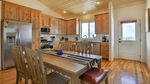 Une cuisine moderne dotée de meubles en bois, d’appareils électroménagers en acier inoxydable et d’un coin repas avec une table et des chaises en bois.