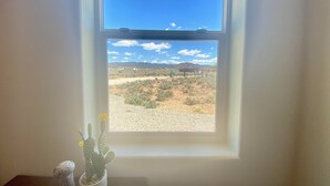Une fenêtre donnant sur un paysage désertique, avec un cactus et une petite figurine posée sur une table.