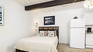 Ein Schlafzimmer mit einem Bett, einem Nachttisch, einer Kommode, einem weißen Kühlschrank und einem gerahmten Bild an der Wand.