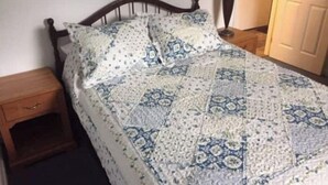 Yhden hengen sänky, jossa on kuviollinen peitto, yöpöytä ja lamppu.