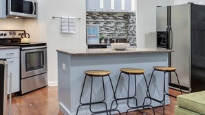 Une cuisine moderne dotée d’appareils électroménagers en acier inoxydable, d’un plan de travail en granit et d’un coin bar avec des tabourets.