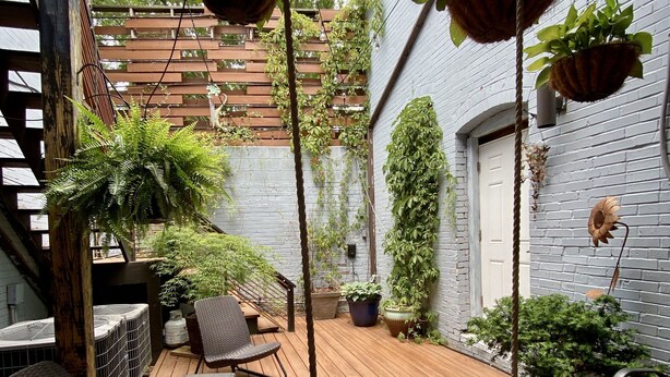 Une terrasse en bois avec des sièges d’extérieur, des jardinières suspendues et un mur en briques.
