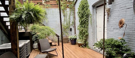 A wooden deck with outdoor seating, hanging planters, and a brick wall.