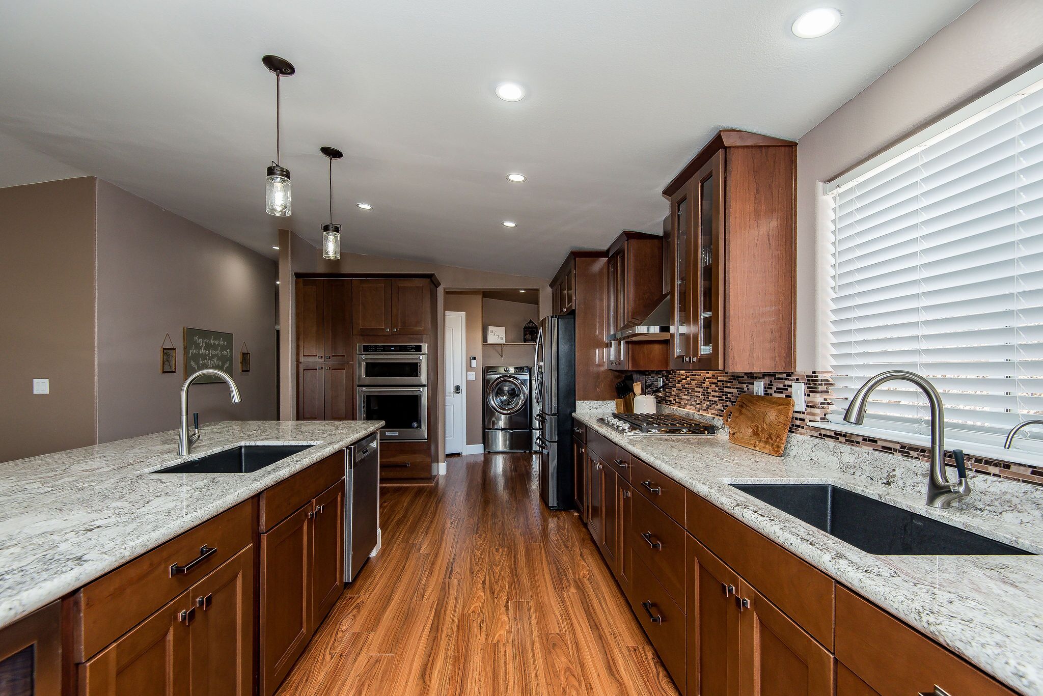 A modern kitchen with wooden cabinets, granite countertops, stainless steel appliances, and pendant lighting.