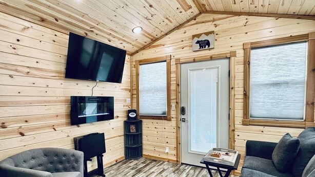 A cabin interior with a television, seating, a door with a window, and a wooden ceiling.