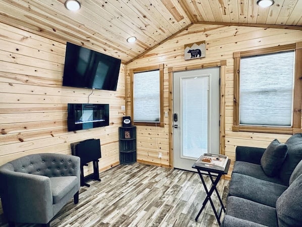 Ein Innenraum einer Hütte mit Fernseher, Sitzgelegenheiten, einer Tür mit Fenster und einer Holzbalkendecke.