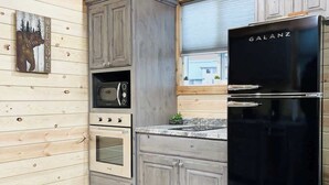 A kitchen with wooden walls, a black refrigerator, a microwave, an oven, and a sink.