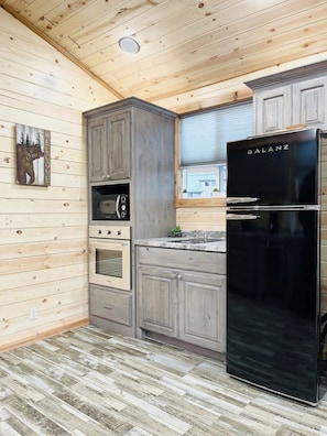 Eine Küche mit Holzwänden, einem schwarzen Kühlschrank, einer Mikrowelle, einem Backofen und einem Spülbecken.