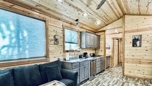 A cabin interior with a sofa, kitchen, and wooden walls.