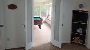 A room with a pool table, a bookshelf with a globe and a dragon, and a door leading to another room with a window and a bench. - ADA King near Crabtree, PNC Arena, State Fairgrounds, NCMA (Raleigh)