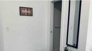 Un pasillo con un cartel que dice 'gather', una mesa negra con una planta y un espejo en la pared.