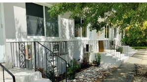 Un edificio residencial con fachada blanca, un camino de hormigón y una escalera de metal con barandilla decorativa.
