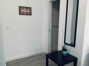 Un pasillo con un cartel que dice 'gather', una mesa negra con una planta y un espejo en la pared.