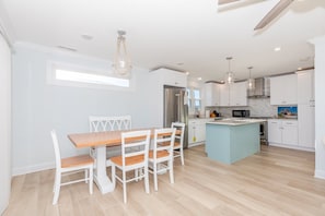 Una cocina moderna con muebles blancos, una isla central y un comedor con mesa de madera y sillas blancas.