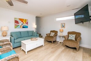Una sala de estar con un sofá, dos sillones, una mesa de centro, un televisor montado en la pared y un cuadro.