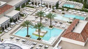 A rooftop pool area with multiple pools, sun loungers, and palm trees.